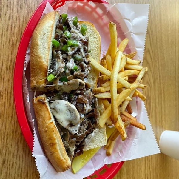 Phillys Cafe & Deli cheesesteak with green peppers, mushrooms, and fries in a red basket.