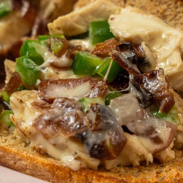 Close-up of a Philly's Cafe & Deli sandwich with melted cheese, green peppers, and onions.