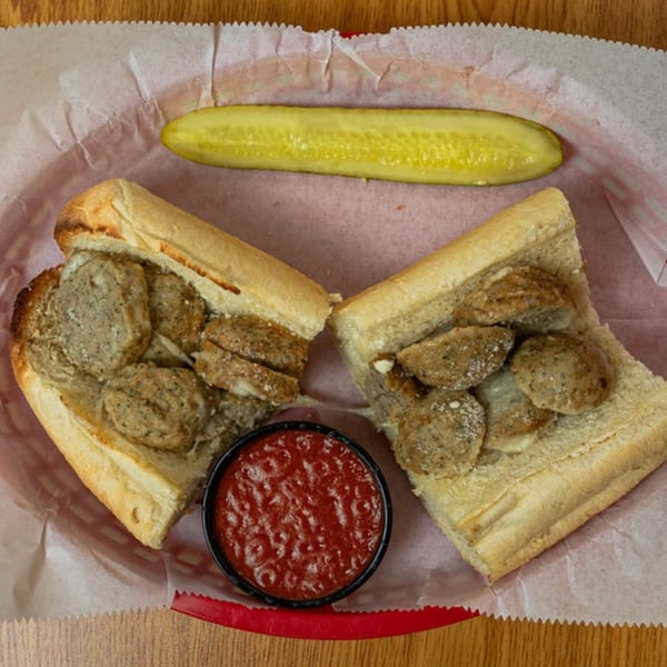 Phillys Cafe & Deli's sausage sandwich, cut in half, with a side of marinara and a pickle spear.