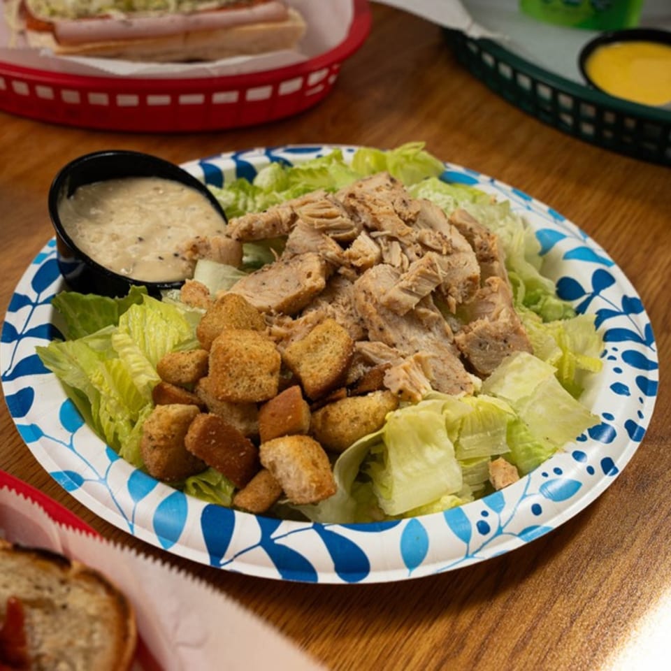 Chicken Caesar salad with croutons and dressing on a blue and white paper plate.