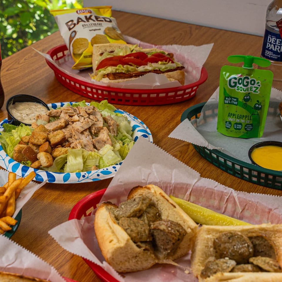 Phillys Cafe & Deli sandwiches, salad, fries, and drinks on a wooden table.