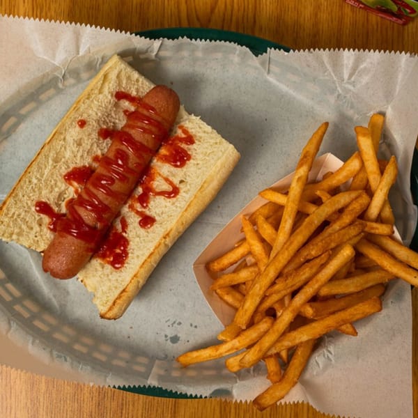 A hot dog with ketchup on a bun, served with a side of french fries in a basket.